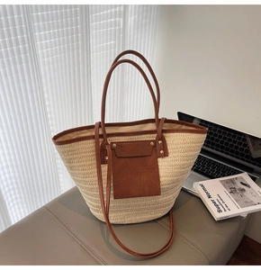 Detail of woven straw tote bag featuring brown leather pocket and metal rivet accents