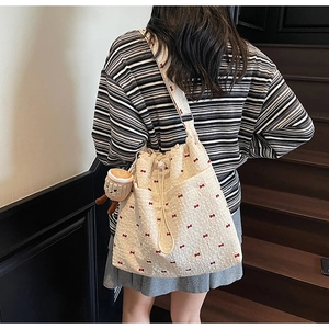 Close-up of cream canvas bucket bag with red bow embroidery and coffee cup charm