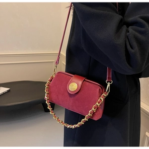 Detail of burgundy suede shoulder bag with gold textured emblem and woven chain strap