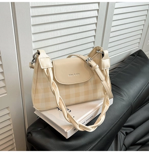Detail of checkered crossbody bag with unique twisted handle on minimalist book display