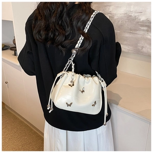 Vue portée épaule d'un sac seau blanc à cordon avec bandoulière chaîne et détail papillon
