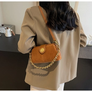 Detailed back view of a brown suede shoulder bag with gold chain strap in a cafe setting