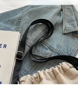 Détail de la bandoulière en nylon noir réglable sur un sac seau beige à cordon