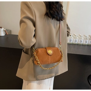 Detail of brown matte suede crossbody bag with gold buckle and chain strap on a model