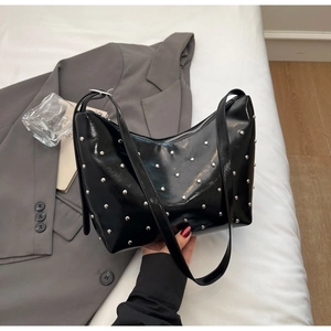 Detail of black croissant bag with silver rivets and polished patent leather surface