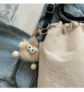 Détail d'un porte-clé monstre en peluche avec bonnet sur un sac seau à cordon tendance