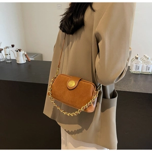 Close-up of brown suede doctor bag featuring vintage gold chain and metallic emblem