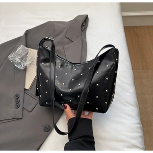 Detail showing high-shine black leather moon bag with silver rivets on a minimalist background