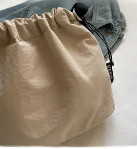 Gros plan d'un sac seau beige à cordon en nylon froissé avec détail du logo KOKO tissé