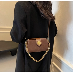 Detail view of brown matte leather bag with golden chain and shield buckle on model