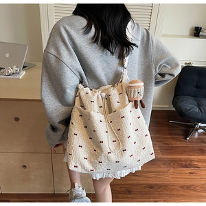 Beige canvas tote bag with red bows worn by model in a cozy home office setting