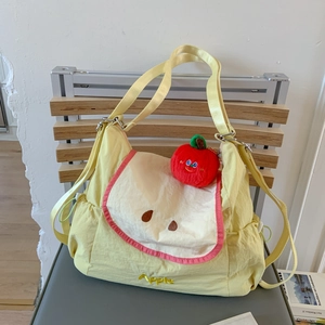 Détail du sac cabas jaune à motif pomme avec un pendentif en peluche rouge vif
