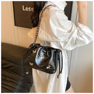 Détail du sac seau noir à cordon avec boucle papillon dorée et bandoulière en chaîne