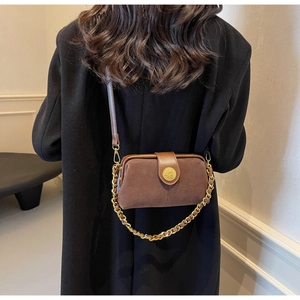 Detail of dark brown suede doctor bag with gold emblem and metal chain strap