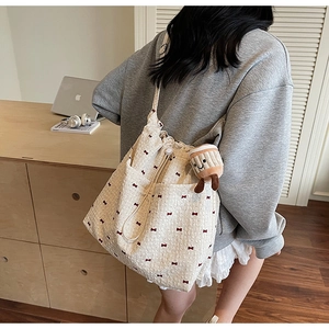 Detail of cream canvas tote bag with red bow print and plush cupcake charm on model