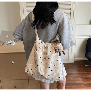 Detail of light beige tote bag with red bow prints, ruffled trim, and a coffee plush charm