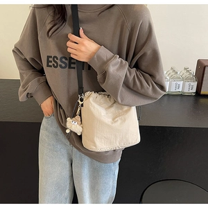 Gros plan d'un sac seau beige à cordon avec charm monstre en peluche et bandoulière noire