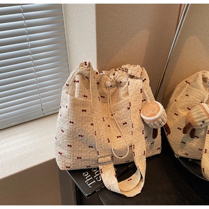 Detailed close-up of cream canvas tote bag featuring red bow patterns and drawstring closure