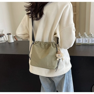 Détail du sac bandoulière vert olive avec cordon et pendentif en peluche sur modèle