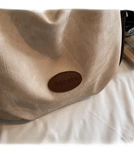 Gros plan sur la texture du tissu beige et le logo en cuir marron du grand sac cabas