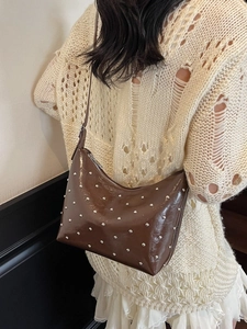 Dark brown patent leather shoulder bag with silver studs and adjustable strap on a model