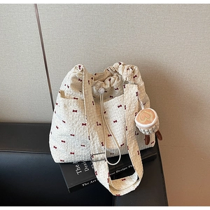 Detail view of waffle fabric tote bag with red bow print and plush coffee cup charm