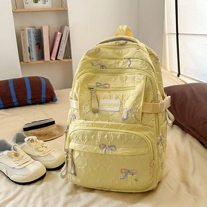 Detail of light yellow backpack showing wrinkled fabric texture and bow embroidery