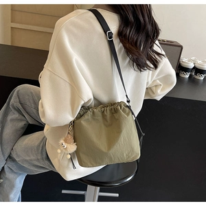 Sac seau vert olive à cordon avec breloque en peluche présenté dans un décor de café