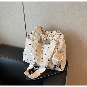 Detail of quilted cream tote bag with red bow print and plush coffee cup pendant