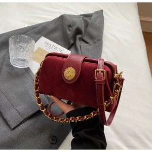 Detail of burgundy doctor bag with suede texture and vintage gold circular emblem