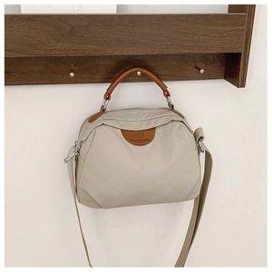 Dettaglio di una borsa in tela beige leggera appesa a un gancio in legno con cuoio