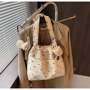 Detail of cream canvas bucket bag with red bow prints and plush cartoon charm