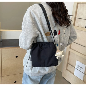 Détail d'un sac bandoulière noir à cordon avec charm en peluche et logo latéral