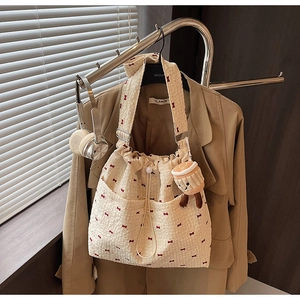 Detail of beige tote bag with red bow prints, drawstring closure and plush pendant