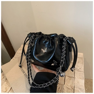 Gros plan du sac seau en cuir verni noir avec fermoir papillon argenté et bandoulière