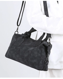 Detail view of a charcoal gray matte crossbody bag on a white textured suit jacket