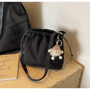 Détail du sac seau noir à cordon avec breloque monstre en peluche sur une pierre