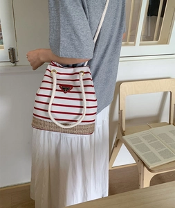 Dettaglio di una borsa a secchiello a righe rosse e bianche con manici in corda e base intrecciata