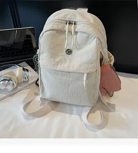 Detailed view of the beige nylon backpack showing the large front zipper pocket and side pouch
