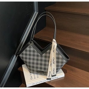 Detail of grey plaid tote bag with V-shaped rim, leather handles, and fashion metal plaque