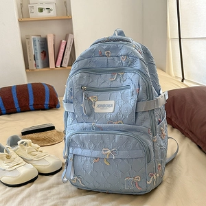 Detail of light blue nylon backpack featuring colorful bow embroidery and side buckles