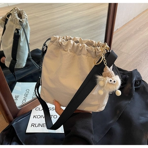 Gros plan sur un sac seau beige à cordon avec pendentif en peluche et bandoulière