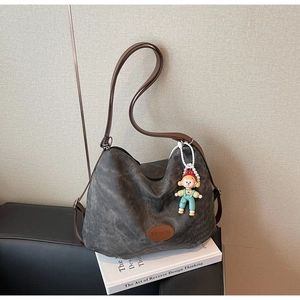 Détail du sac hobo en toile gris foncé avec bandoulière en cuir brun et breloque poupée