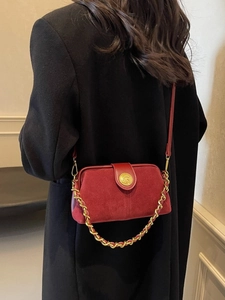 Red suede crossbody bag with gold chain and elephant logo over a black coat