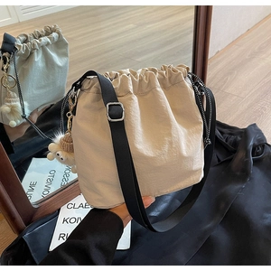 Détail du sac seau beige à cordon avec bandoulière noire et pendentif en peluche doux