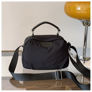 Dettaglio borsa a tracolla in nylon nero con tracolla regolabile e logo in pelle su vetro