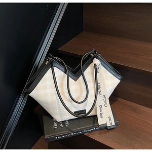 Close-up of beige plaid tote bag with black leather handles and branded woven strap detail