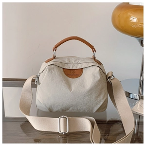 Dettaglio della borsa in nylon beige con manici in pelle marrone e tracolla regolabile