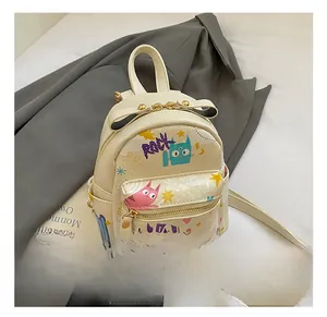 Detail of a beige graffiti mini backpack featuring cute cartoon cat prints and bow