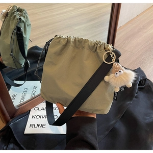 Détail du sac seau en nylon vert avec bandoulière noire et pendentif monstre en peluche